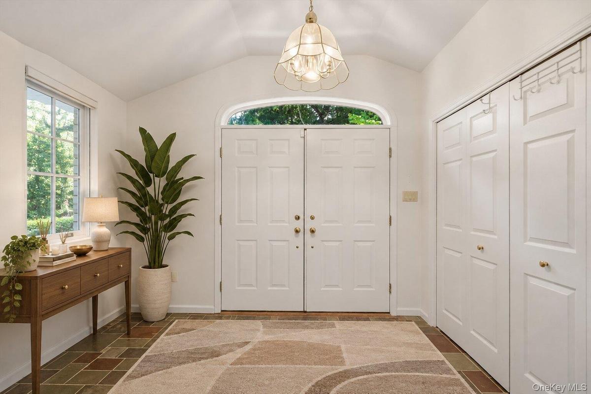Spacious entry foyer featuring double doors, natural light, a vaulted ceiling, and convenient storage closets.