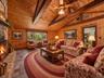 Virtually staged family room highlighting the vaulted wood ceiling, exposed beams, stone fireplace, and generous seating area.