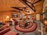 Virtually staged family room showcasing the spacious layout, architectural beams, and impressive stone fireplace.