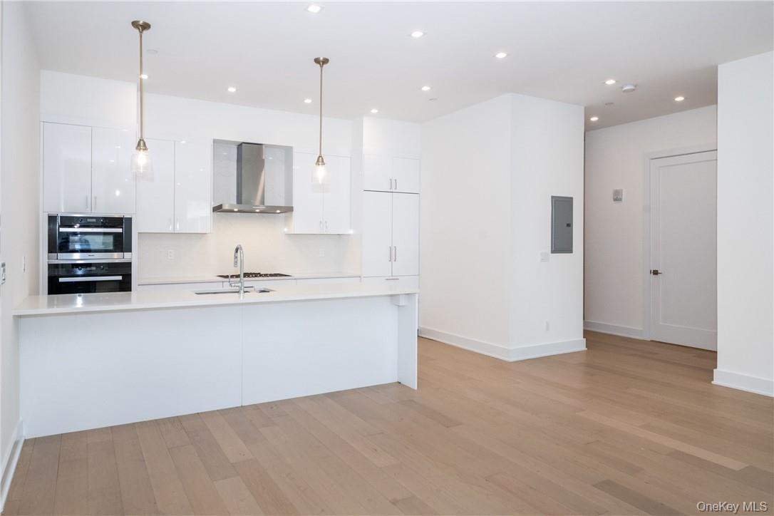 Kitchen featuring light hardwood / wood-style floors, wall chimney exhaust hood, decorative light fixtures, double oven, and white cabinets