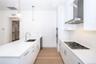 Kitchen featuring stainless steel appliances, wall chimney range hood, decorative light fixtures, white cabinets, and light hardwood / wood-style floo