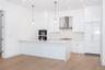 Kitchen featuring stainless steel double oven, wall chimney range hood, white cabinetry, light wood-type flooring, and decorative light fixtures