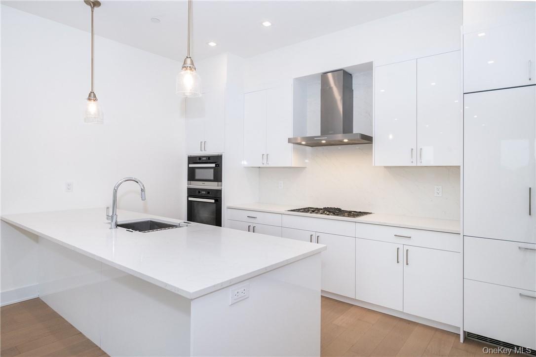 Kitchen featuring white gas stovetop, white cabinets, wall chimney exhaust hood, sink, and pendant lighting