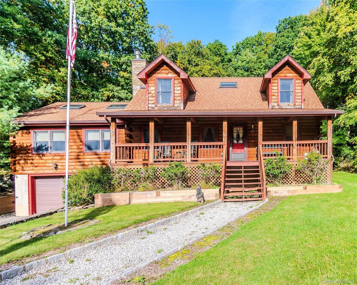 Log-style siding exterior with a covered front porch, dormer windows, a stone chimney, and a lower-level garage