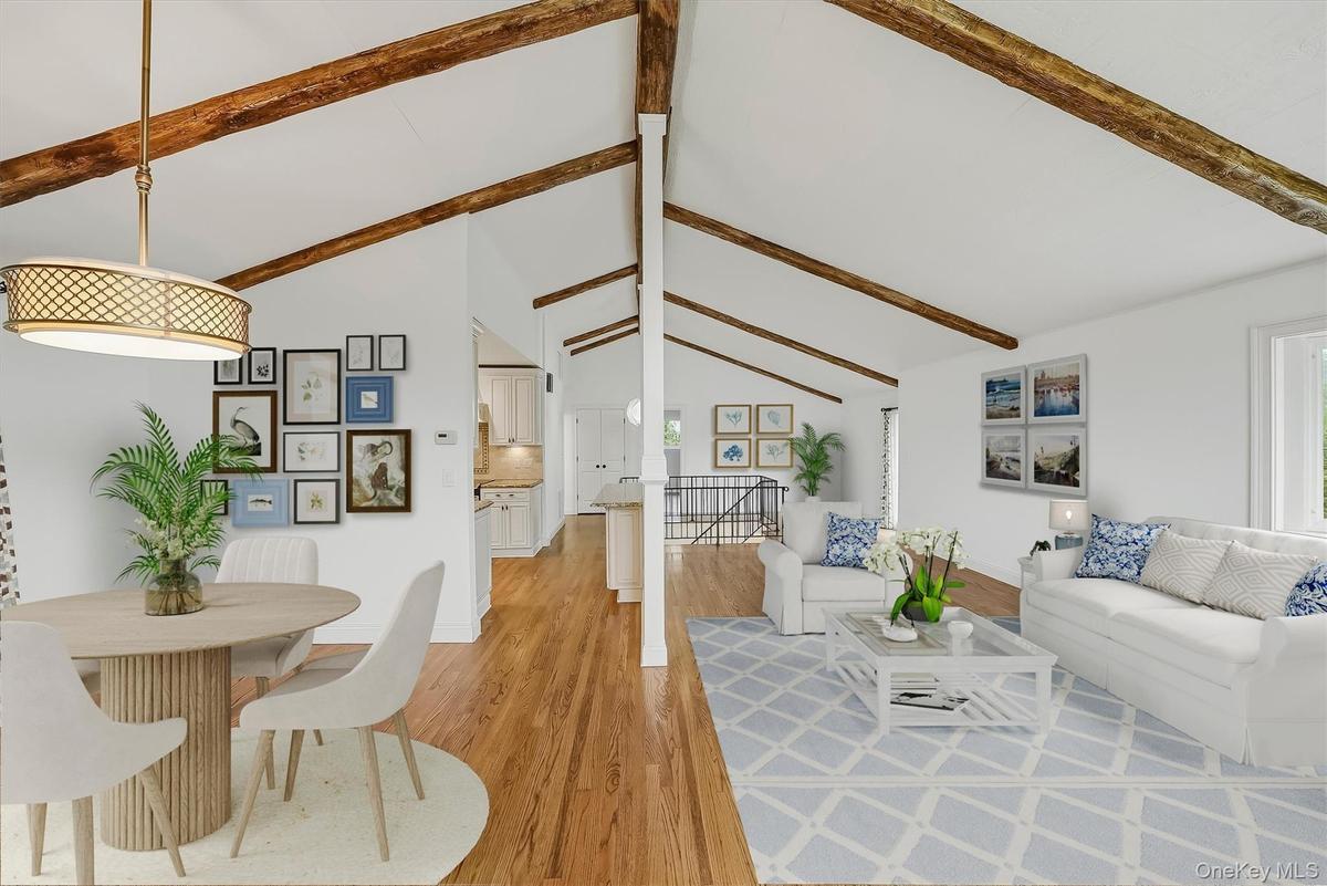 Virtually staged open-plan great room w/ hardwood floors, exposed wood beams, and fresh paint.
