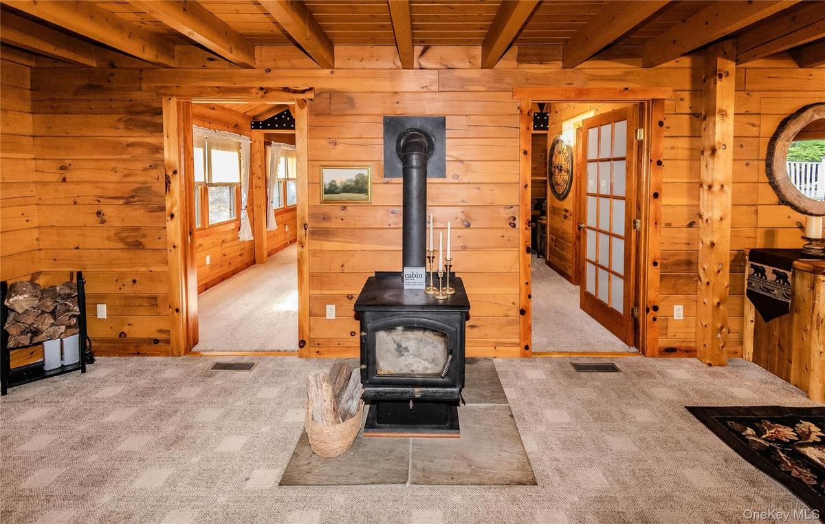 Wood paneling throughout, exposed wood beam ceiling, central wood-burning stove, and two frosted glass French doors