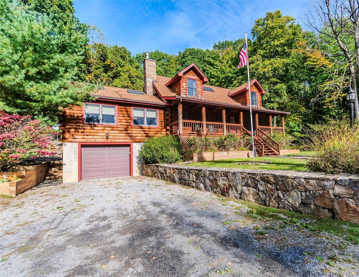 Log cabin exterior with a covered porch, dormer windows, and a prominent stone chimney
