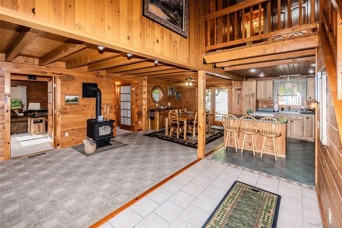Wood-paneled interior featuring a wood-burning stove, exposed wood beam ceiling, and a kitchen with wood cabinetry