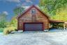 Log cabin exterior with a pitched roof, a paneled garage door, an upper-level window, and an attached covered carport