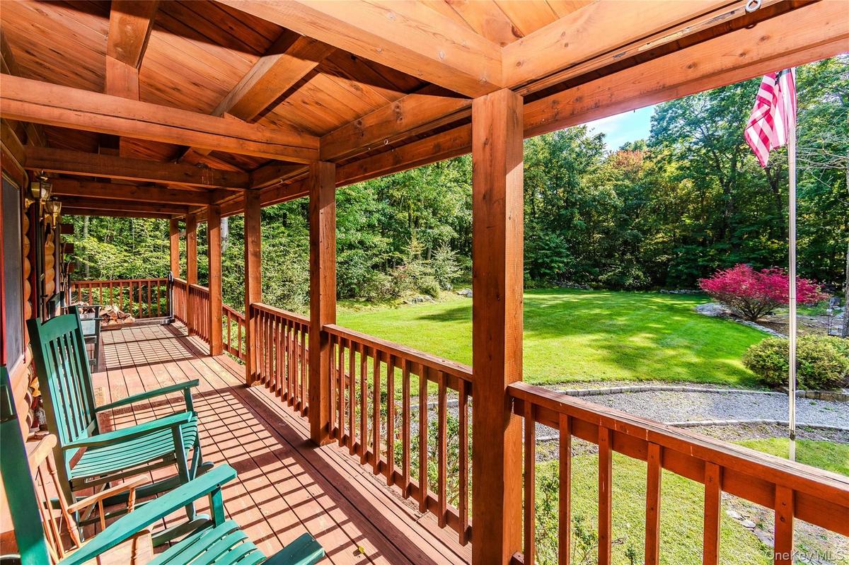 Expansive covered porch featuring wood flooring, wood beam ceiling, wood railings, and a manicured lawn