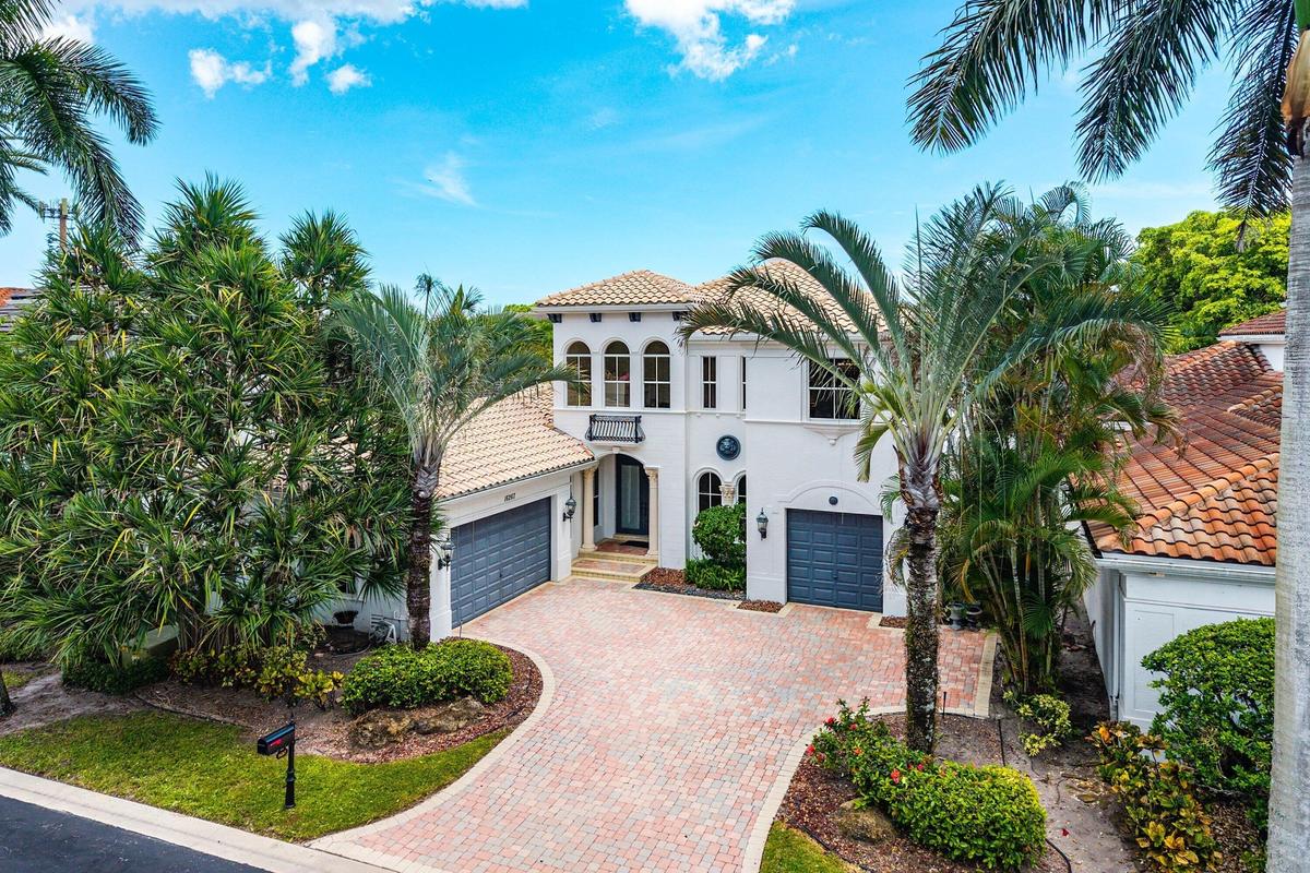Mediterranean-inspired architecture, modern color palette, with a barrel tile roof, arched windows, a paver driveway, and mature landscaping