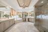 Marble flooring with accent details, dual vanities with integrated sinks, recessed jetted bathtub, glass-enclosed shower, and a decorative tray ceilin