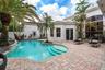 Curved swimming pool with waterfall feature, surrounded by a multi-tone paver patio and tropical landscaping