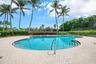 Freeform swimming pool with integrated steps, surrounded by paver decking and mature landscaping with palm trees