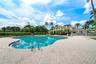Curved swimming pool with a paver deck, surrounded by manicured landscaping and palm trees