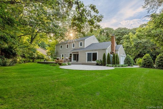 Spacious backyard featuring a manicured lawn, mature trees, a paver patio, and a brick chimney