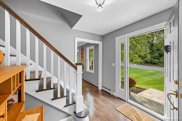 Wood-finish flooring, staircase with white risers and wood treads, white banister with wood handrail, paneled door with glass insert, and a stone pave