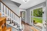 Wood-finish flooring, staircase with white risers and wood treads, white banister with wood handrail, paneled door with glass insert, and a stone pave