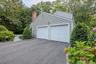 Side entry two-car garage with panel doors, asphalt driveway, brick chimney, and mature perimeter landscaping