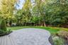 Expansive backyard featuring a curved paver patio, lush green lawn, and mature trees