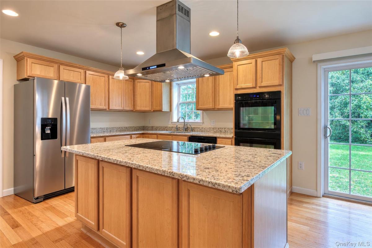 Kitchen featuring light wood cabinetry, granite countertops, stainless steel appliances, a center island with cooktop, and hardwood flooring