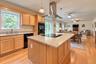 Open-concept kitchen featuring an island with a built-in cooktop, granite countertops, wood-finish flooring, light wood cabinetry, and a stainless ste