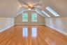 Bedroom featuring wood-finish flooring, two large skylights, two double-hung windows, a ceiling fan with integrated lighting, and sloped ceilings
