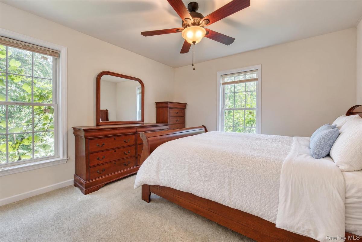 Neutral-toned walls, two large windows, a ceiling fan with integrated lighting, and carpeted flooring