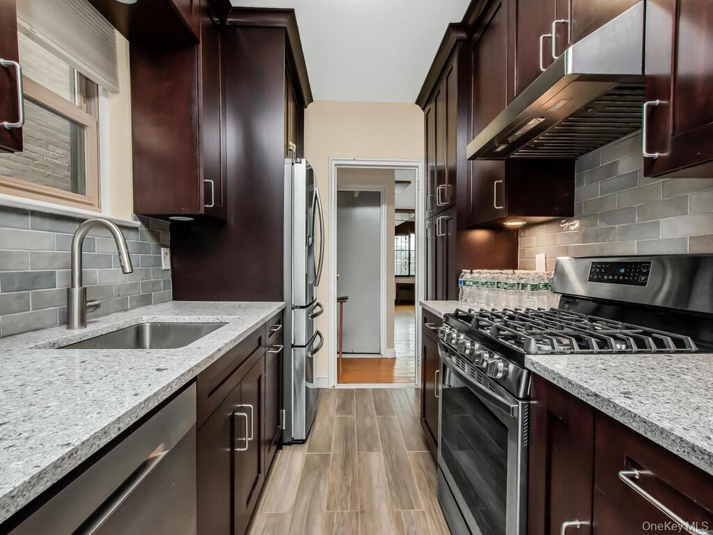 Kitchen with under cabinet range hood, a sink, tasteful backsplash, stainless steel appliances, and light stone countertops