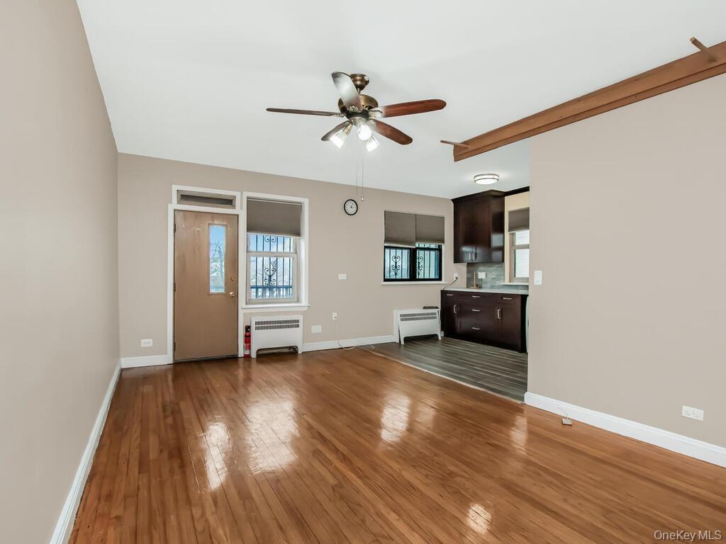 Unfurnished living room featuring baseboards, wood-type flooring, a ceiling fan, and radiator heating unit