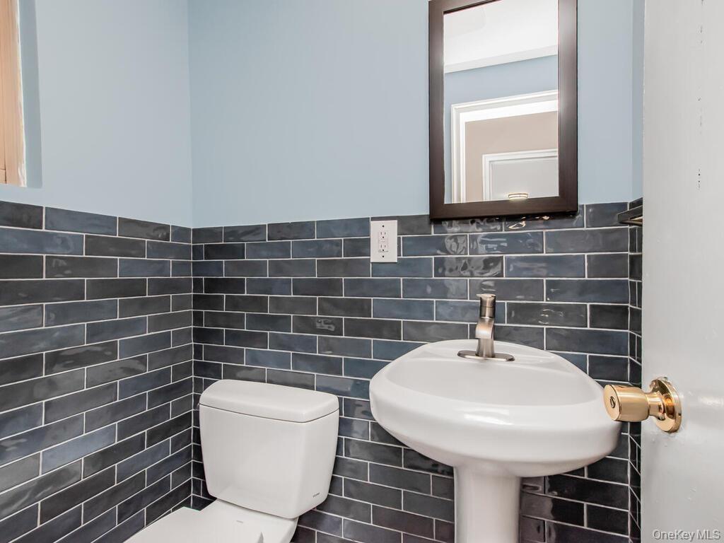 Half bathroom with toilet, tile walls, and wainscoting