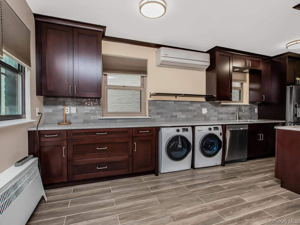 Kitchen featuring backsplash, wood tiled floor, a wall unit AC, appliances with stainless steel finishes, and washer and dryer