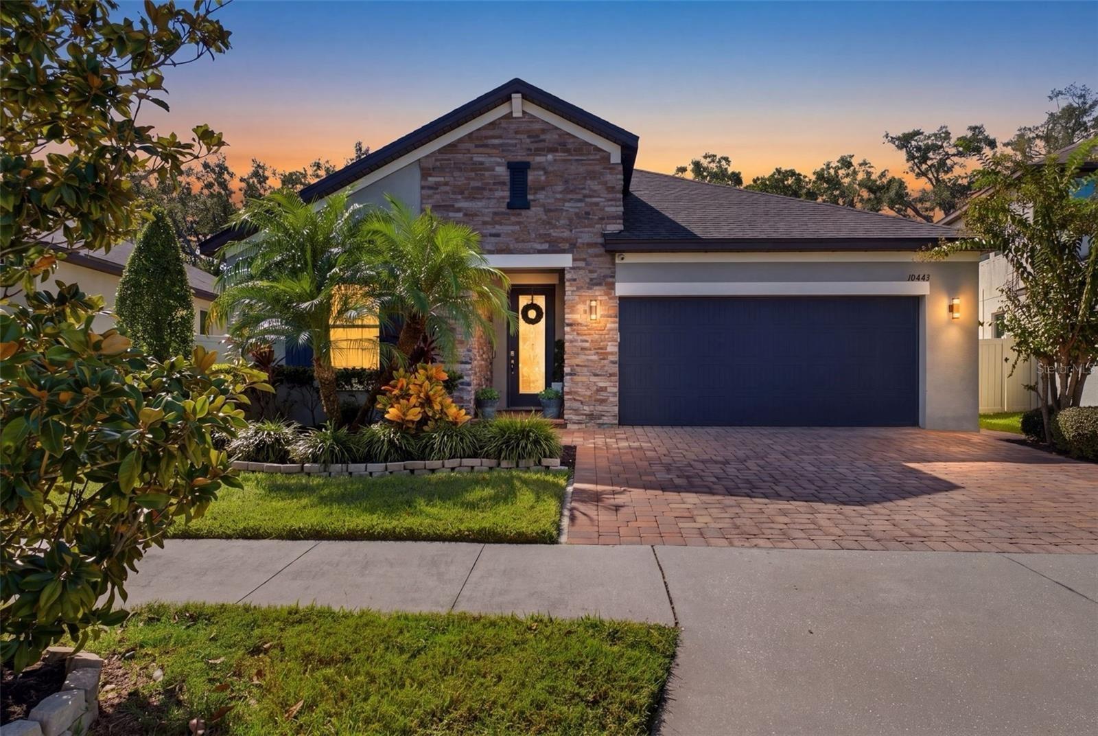 Twilight view with extended paver driveway and landscape lighting