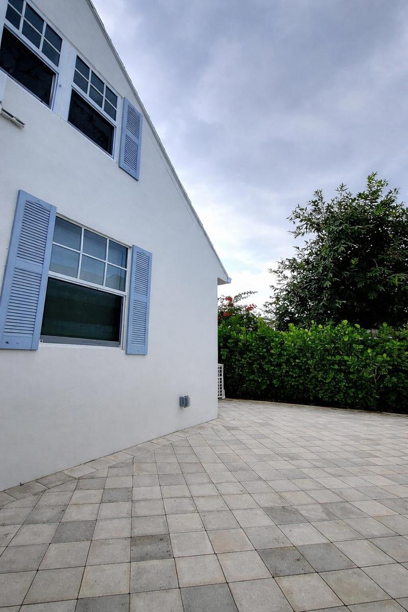White exterior with blue louvered shutters, multi-pane windows, and a paved courtyard