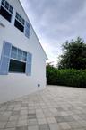 White exterior with blue louvered shutters, multi-pane windows, and a paved courtyard