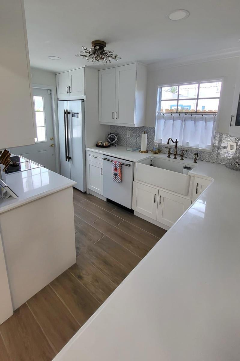 White shaker cabinetry, wood-finish flooring, white countertops, built-in dishwasher, and a farmhouse sink with a wall-mounted faucet