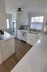 White shaker cabinetry, wood-finish flooring, white countertops, built-in dishwasher, and a farmhouse sink with a wall-mounted faucet
