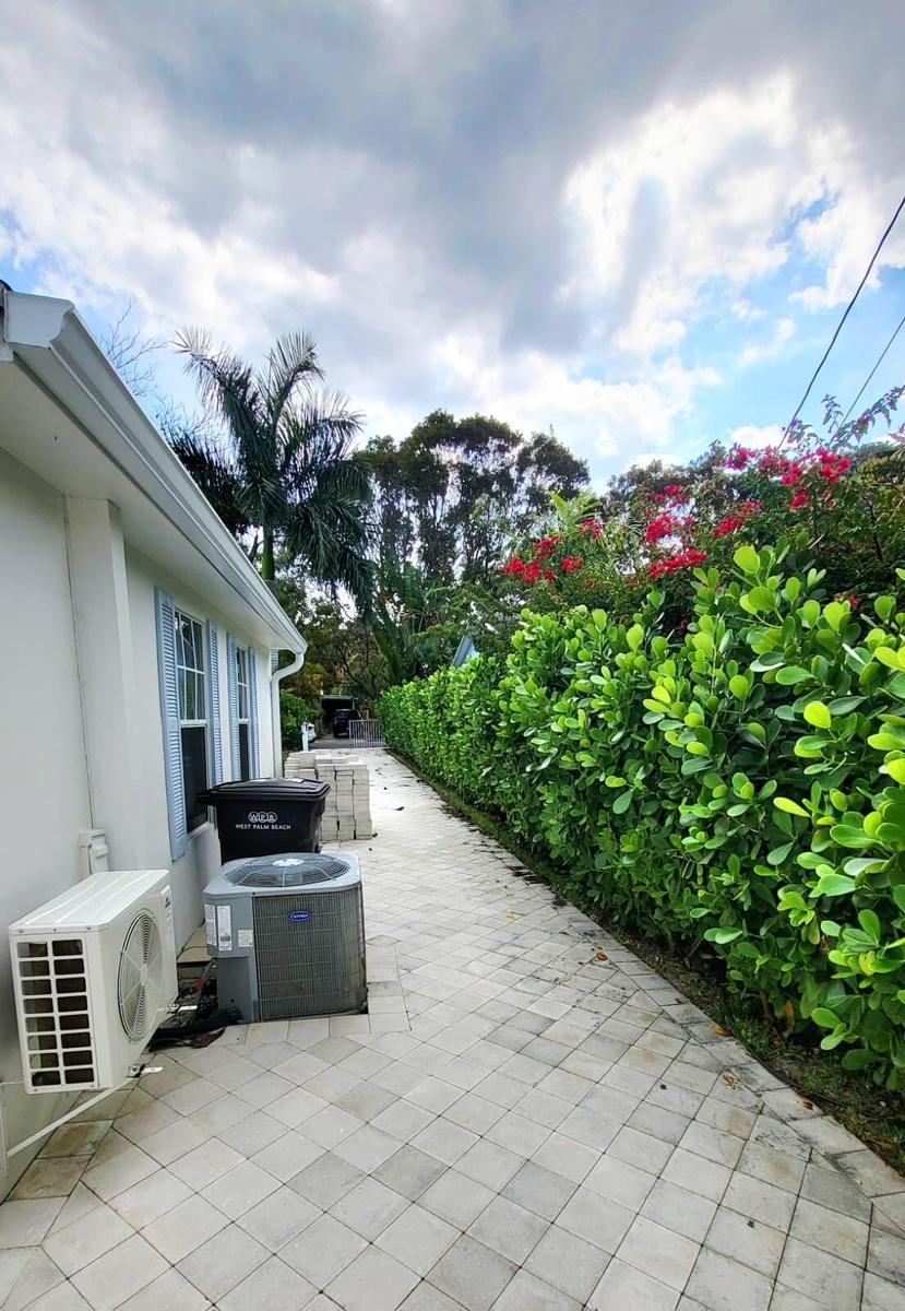 Paver pathway alongside a lush green hedge and flowering shrubs