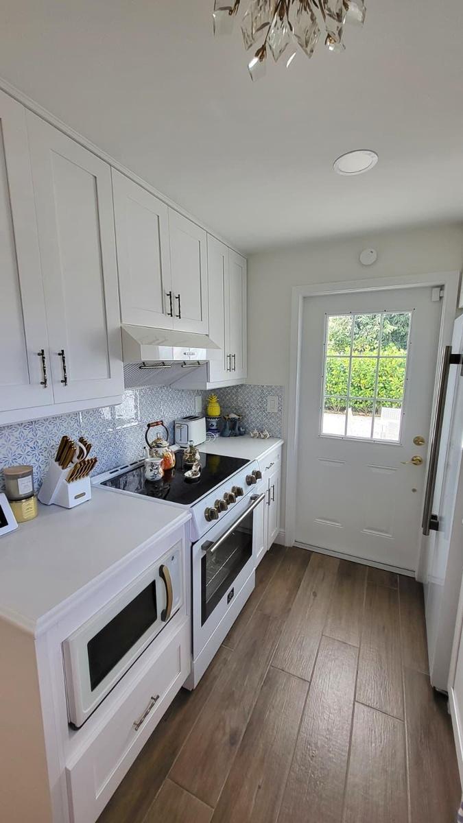 White cabinetry, light-toned countertops, full tile backsplash, wood-finish flooring, and a glass-paned door