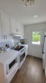 White cabinetry, light-toned countertops, full tile backsplash, wood-finish flooring, and a glass-paned door