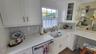 White shaker-style cabinetry, patterned tile backsplash, farmhouse-style sink with a brass-finish faucet, and a built-in dishwasher