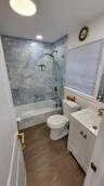 Bathroom featuring wood-finish flooring, a white vanity with integrated sink, a white bathtub, and a tiled shower surround