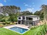 Modern architectural exterior with a private swimming pool, expansive wood-finish decking, floor-to-ceiling windows, and mature perimeter landscaping