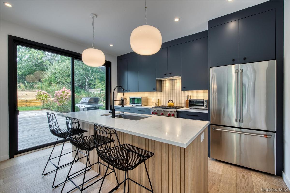 Kitchen featuring a large center island with a light-toned countertop, dark blue cabinetry, stainless steel French door refrigerator, and a gas range
