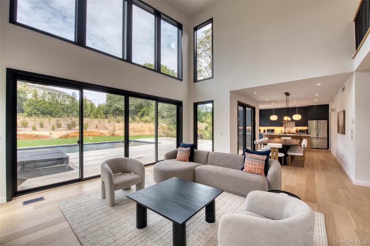 Double-height living area with expansive sliding glass doors, upper transom windows, and light wood-finish flooring