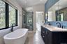Freestanding soaking tub with black fixture, glass-enclosed shower, dual vanity with undermount sinks, and blue tiled accent wall