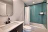 Bathroom featuring a dark wood-finish vanity with a white countertop and rectangular sink, matte black faucet, and a shower/tub combination with teal 