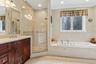 Built-in jetted tub with tile surround, corner glass-enclosed shower with tile, dark wood-finish vanity with countertop, undermount sink, and recessed