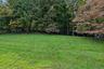Expansive green lawn with mature trees and a partial wood fence