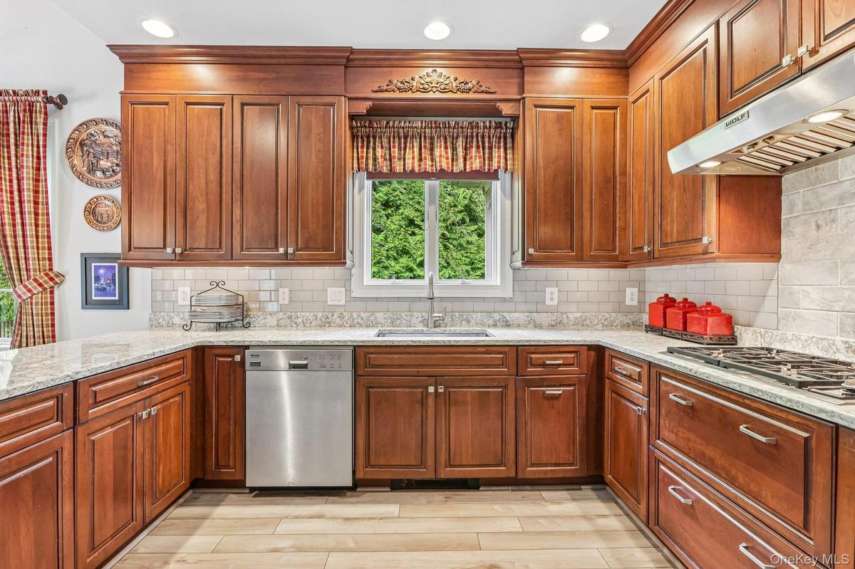 Cherry wood cabinetry, light-toned countertops, subway tile backsplash, stainless steel dishwasher, and a gas cooktop